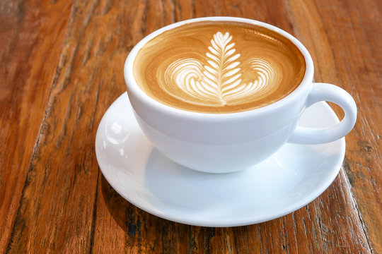 Hot coffee latte cappuccino cup with beautiful 'rosetta' latte art milk foam on rustic wood table background.