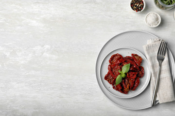 Plate of sun dried tomatoes on light table, flat lay composition with space for text