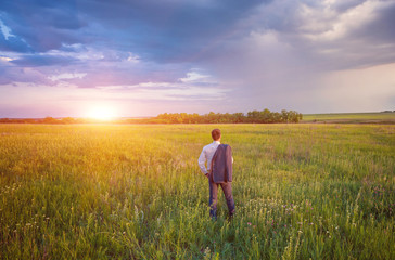Naklejka na ściany i meble Businessman in elegant suit with his jacket hanging over his shoulder standing in field