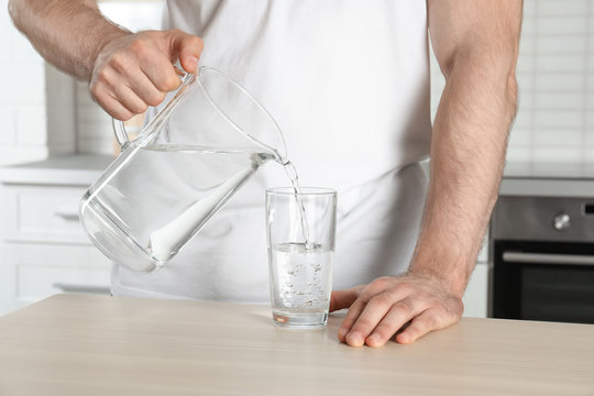 Man pouring water into glass at table, closeup