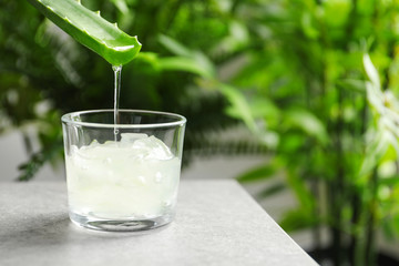 Aloe vera juice dripping from leaf into glass on table against blurred background with space for...