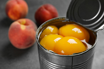 Tin can with conserved peach halves on table, closeup