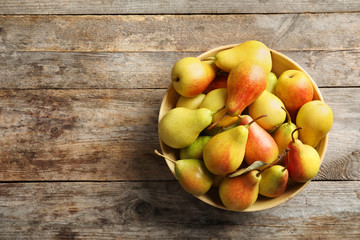 Bowl with ripe pears on wooden background, top view. Space for text