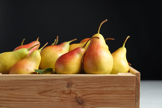 Wooden crate with ripe pears on black background, closeup