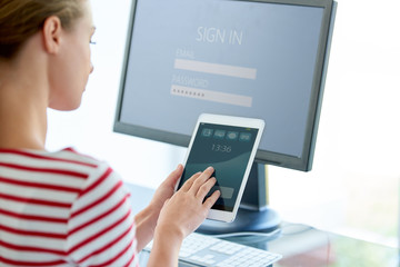 Rear view shot of young businesswoman sitting in front of laptop and using her digital tablet in the office. 