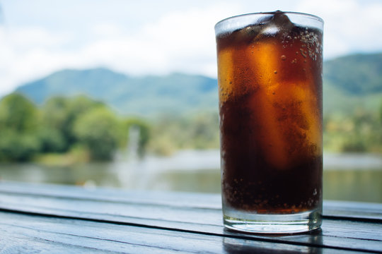 Cola in glass on table with mountain and river background