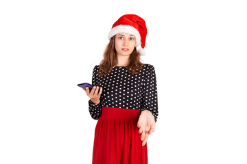 Portrait of a confused cute girl in dress pointing at mobile phone. emotional girl in santa claus christmas hat isolated on white background. holiday concept