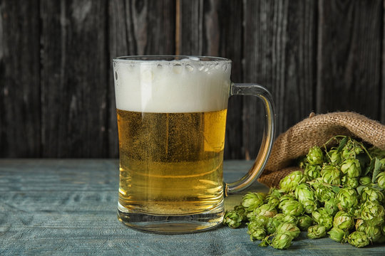 Composition with tasty beer and fresh green hops on wooden table