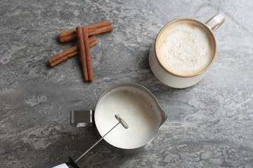 Milk frother over pitcher near cup of coffee and cinnamon sticks on table