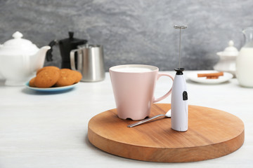 Board with milk frother and cup on table. Space for text