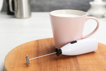 Board with milk frother and cup on table. Space for text