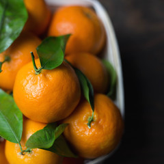 Mandarins with leaves in a wooden box on a wooden black background, top view