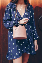 street style fashion details. close up, young fashion blogger wearing a floral dress, and a black and white analog wrist watch. checking the time, holding a beautiful pink purse.