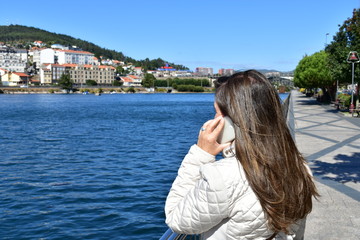 Fototapeta na wymiar Woman talking on the phone. River and walking area with trees and blue sky. Pontevedra, Spain.