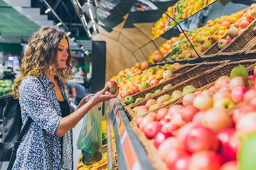 young adult woman choosing apples in grocery store