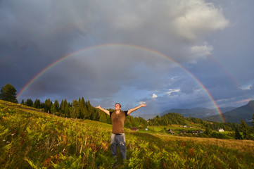 A happy man enjoys the rainbow in the mountains.