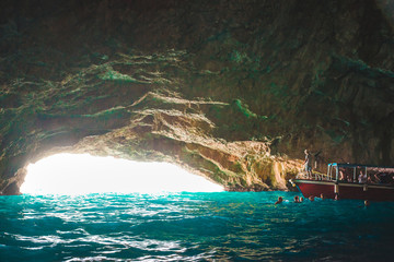 boat with group of tourists in beautiful grotto with azure transparent water - obrazy, fototapety, plakaty