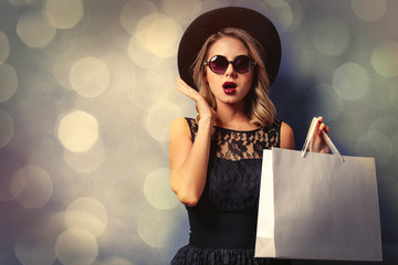 Portrait of a young style girl in black dress and hat with shopping bags on gray background with bokeh