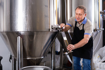 Brewer is checking the quality of beer in flask indoor.