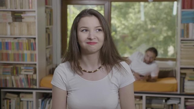 Awkward reaction of young woman doing funny grimaces and gestures fooling around with boyfriend behind her