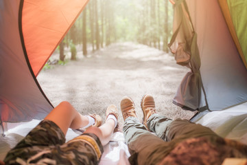 Couple lie down in tent stretching their legs looking at the view of forest outside the camping...