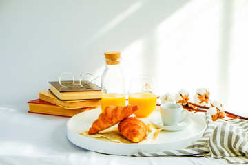 Morning breakfast in bed, white tray with glass of fresh orange juice, cup of coffee and french croissant, vintage eye glasses and books, stripped blankets. Close up, top view, background, copy space.