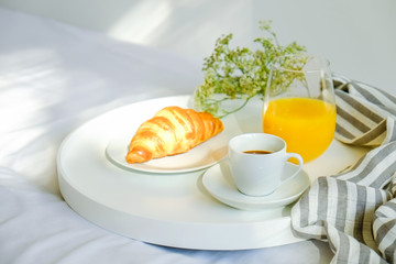 Breakfast in bed concept. White tray with glass half full of fresh orange juice, cup of coffee and french croissant bagel, stripped blankets. Close up, top view, background, copy space.