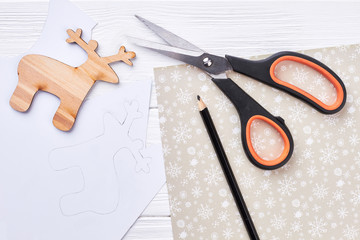 New Year handmade craft materials. Scissors, pencil, carved wooden deer, draw of deer on paper, top...