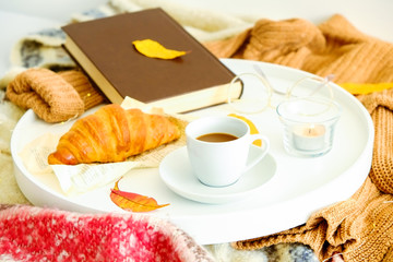Morning breakfast in bed, white tray with cup of coffee and french croissant, vintage eye glasses and book, yellow autumn leaves, november mood. Close up, top view, background, copy space.