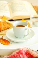 Morning breakfast in bed, white tray with cup of coffee and french croissant, vintage eye glasses and book, yellow autumn leaves, november mood. Close up, top view, background, copy space.