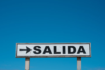 Exit sign (spanish: SALIDA) isolated on blue sky  