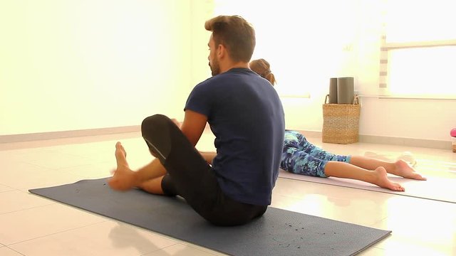 Yogis practicing Ashtanga Mysore style in bright studio. Young man in janu sirsasana and woman doing vinyasa. Students perform yoga sitting postures. Demanding effort, discipline, tired concepts