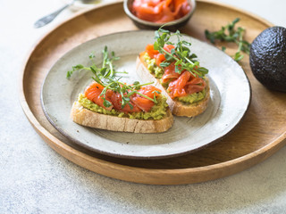 Toasts with avocado and salted salmon with fresh pea sprouts on a plate on a wooden tray