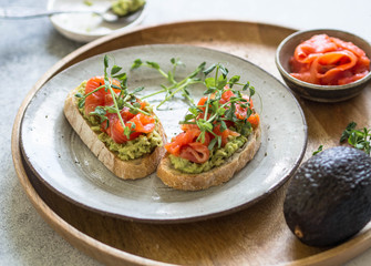 Toasts with avocado and salted salmon with fresh pea sprouts on a plate on a wooden tray