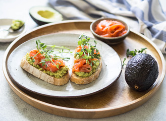 Toasts with avocado and salted salmon with fresh pea sprouts on a plate on a wooden tray