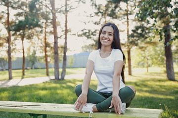 Naklejka na ściany i meble Young beautiful woman sitting on bench in park. Pretty girl at outdoors on summer day. Nature environment background.