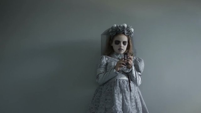 Girl in a suit and with the makeup of a dead bride is sorting a bunch of old keys in her hand. Selects one and approaches the camera to open the lock. Halloween scene