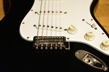 Black and white electric guitar body closeup. Bridge, single coil pickups, pickguard, knobs and jack.