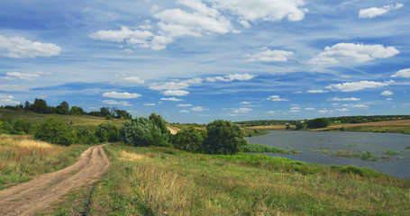 Fototapeta na wymiar Sunny summer landscape with ground country road,river and beautiful clouds in blue sky.Tula region,Russia.