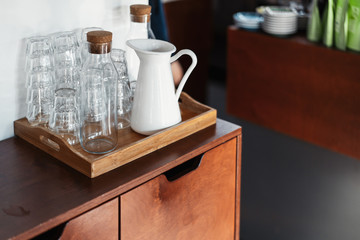 Transparent glasses and white metal jar on wooden cupboard in cafe.