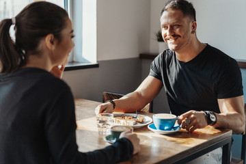 Young couple sitting in cafe at date, drinking coffee and eating dessert.