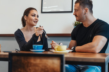 Young couple sitting in cafe at date, drinking coffee and eating dessert.
