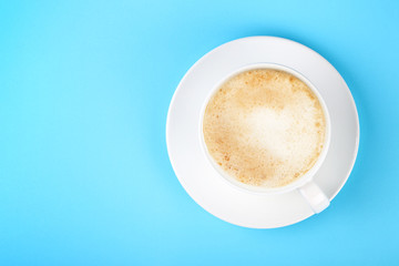 Full white cup of cappuccino coffee on blue