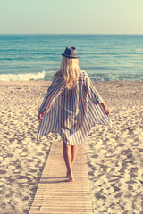 Rear view of a beautiful, blond young girl looking at the sea. Concept of freedom, holiday, beach, clear sky background. Horizontal view.