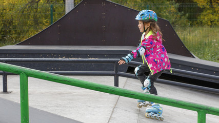 Little girl riding on roller skates in a helmet and knee pads