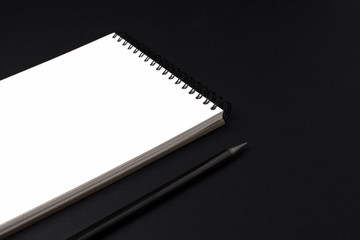 Opened clean notebook or sketchbook with pencil on black background