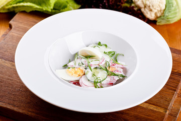 Salad with egg, radish, cucumber and sour cream on white plate. Close up
