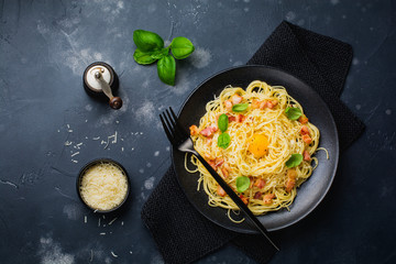Pasta spaghetti carbonara with bacon, parmesan cheese, egg yolk and basil leaves on black background. Traditional Italian dish. Top view.