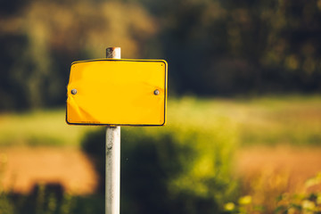 Empty yellow road sign banner on pole with blurred green trees on background 