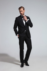man in tuxedo fixing his bowtie and looks to side